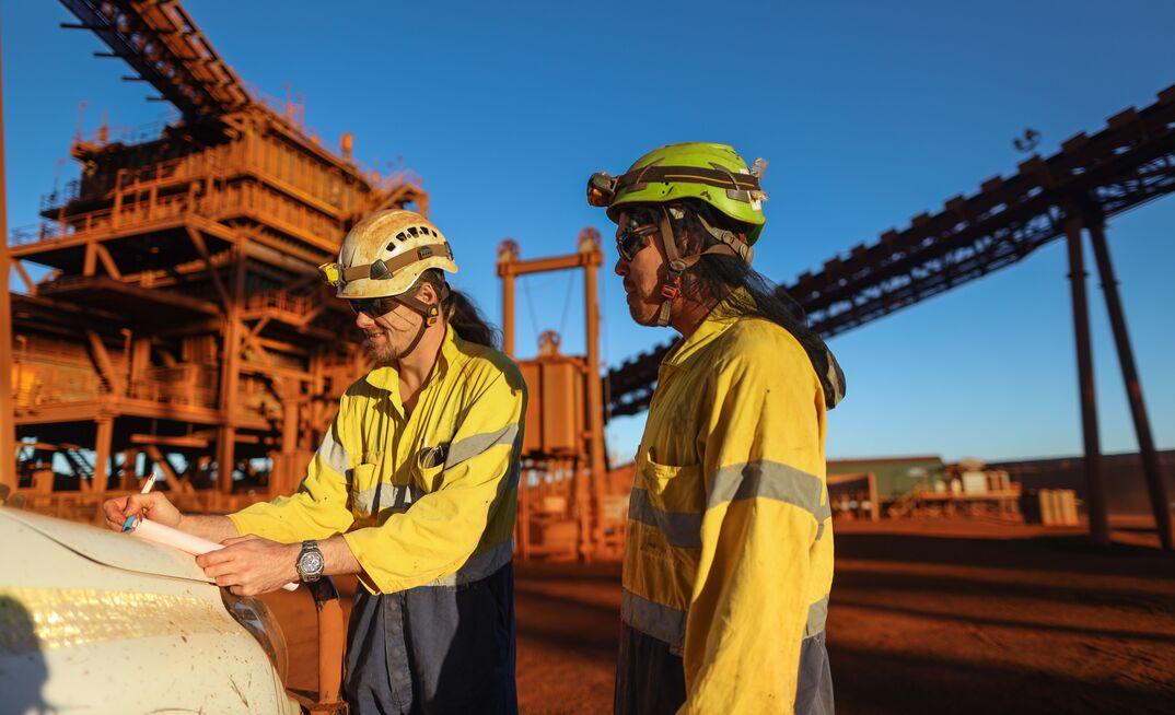 Trade assistants reviewing a work pack in front of a mine site processing plant